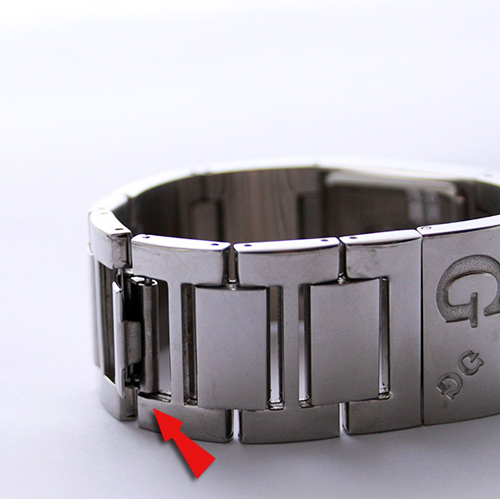 Mécanisme d'attache d'un bracelet de montre en métal avec flèche rouge indiquant l'axe
