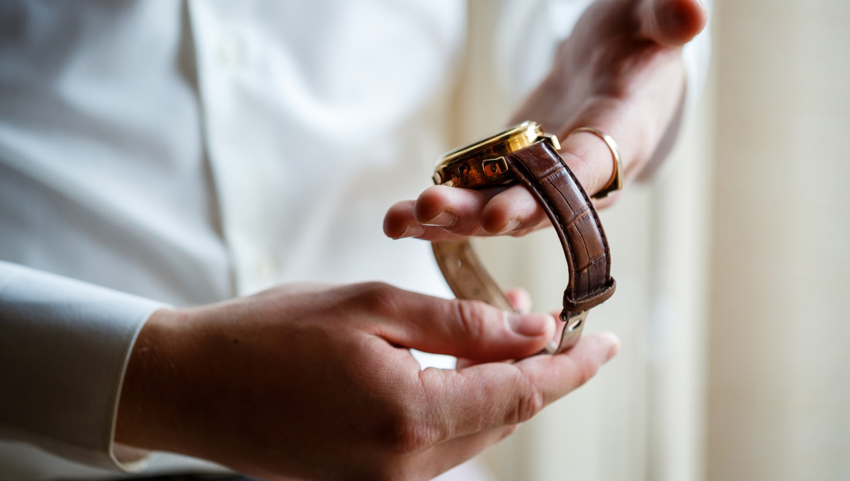 Mains tenant et examinant une montre avec boîtier doré et bracelet en cuir marron