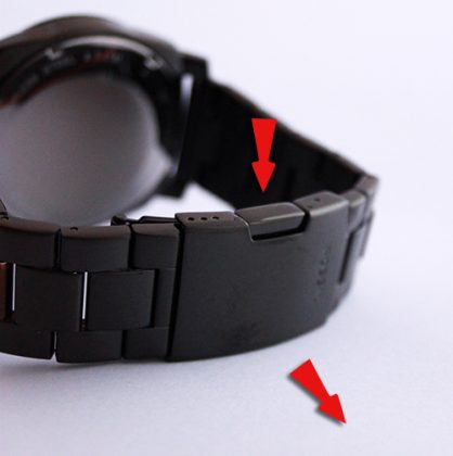 Détail du fermoir noir d'un bracelet de montre, montrant les points de pression pour l'ouvrir