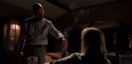 Walter White debout parlant à Skyler assise dans une pièce sombre et enfumée