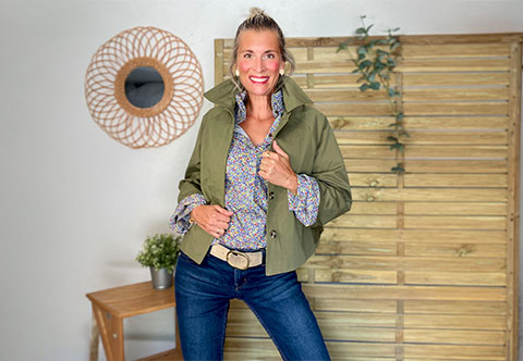 Femme souriante en veste kaki, chemise fleurie, jean bleu et ceinture beige